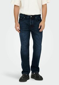 Jeans de mezclilla azul oscuro con corte recto, diseño de cinco bolsillos y una cinturilla resistente con costuras visibles y detalles de metal.