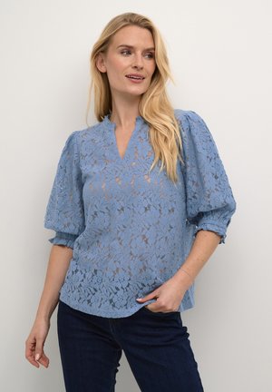 Helles blaues Spitzenbluse mit floralem Muster, kurzen Puffärmeln, V-Ausschnitt und lockerer Passform. Kombination mit dunklen Jeans.