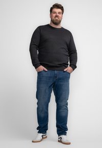 Pulover gri închis cu decolteu rotund, de grosime medie, asortat cu blugi albaștri. Modelul poartă adidași albi cu accente negre.