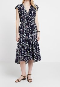 Blommig midiklänning med marinblå bakgrund, V-ringning, korta ärmar och rynkad midja. Lätt tyg med flerfärgade blommönster.