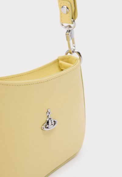 Κίτρινη δερμάτινη τσάντα χειρός με καμπυλωτό σχήμα, διακοσμημένη με αξεσουάρ σε ασημί τόνο και αποσπώμενο λουράκι. Λεπτή υφή και μινιμαλιστικός σχεδιασμός.