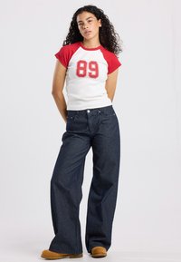 White and red short-sleeve shirt with the number 89, paired with navy striped wide-leg jeans and brown shoes.