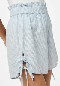 Mėlynos ir baltos langelių šortai su elastine juostele ir banguotu kraštu. Yra šoninės plyšio detalės su raišteliais reguliavimui. Minkšta tekstūra.