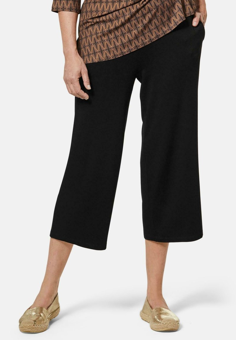 Pantalons noirs coupés en tissu doux, avec une coupe décontractée et une coupe droite, associés à des espadrilles dorées.