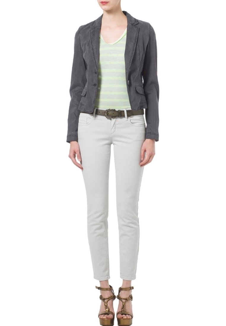 Szary żakiet na lekko zielonym paskowanym topie, w połączeniu z białymi, dopasowanymi spodniami i brązowymi sandałami na obcasie. Pasek zdobiony dekoracyjną klamrą.