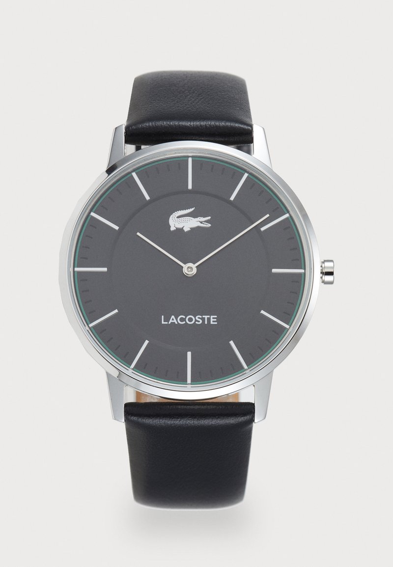 Lacoste klokke med et sølvfarget rustfritt stålhus, svart rund urskive, grønne detaljer, sølvtimeindikatorer og svart lærrem.