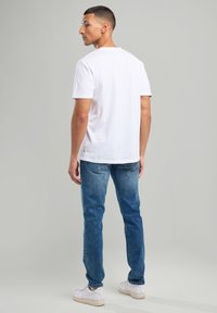 White cotton t-shirt, crew neck, short sleeves. Paired with blue denim jeans, slightly fitted. Shoes are white sneakers. Simple design.