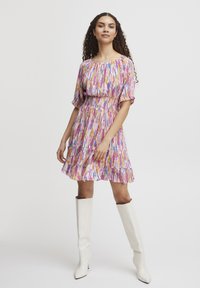 Rochie plisată cu imprimeu abstract multicolor, având mâneci scurte tip puff și un tiv cu volane. Asortată cu cizme albe până la genunchi.