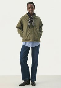 Jachetă cu glugă de culoare verde măslin, cu închidere cu capse, asociată cu o cămașă în dungi albastre și albe și pantaloni din denim închis; cizme negre până la gleznă completează ținuta.