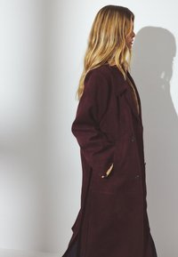Burgundia sametist trench coat, pikad varrukad, topelt nööbid, küljetaskud ja lahtine lõige. Sile tekstuur ja kohandatud krae.