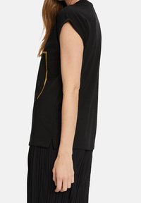 Camiseta negra de manga corta en algodón suave con mangas remangadas y aberturas laterales. Presenta un gráfico minimalista en dorado metálico en la parte frontal.