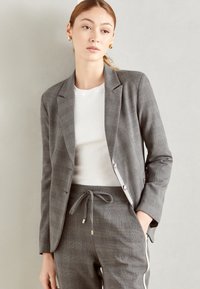 Grijze geblokte blazer met een getailleerd ontwerp, sluiting met één knoop en twee voorkuipen, gecombineerd met een witte T-shirt met ronde hals en bijpassende broek.