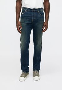 Vaqueros de mezclilla azul oscuro con pierna recta, que cuentan con cinco bolsillos, un cierre de botón metálico y un ligero desgaste a lo largo de los muslos.