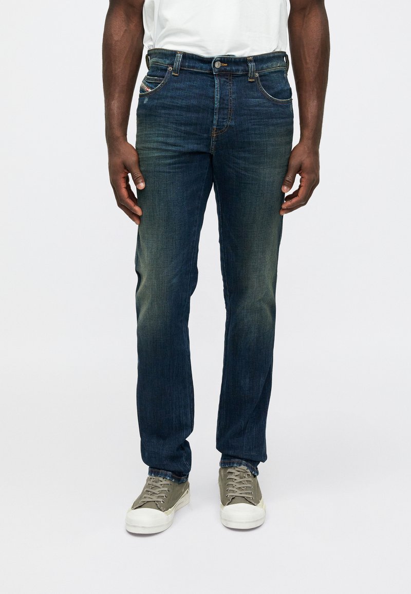 Vaqueros de mezclilla azul oscuro con pierna recta, que cuentan con cinco bolsillos, un cierre de botón metálico y un ligero desgaste a lo largo de los muslos.