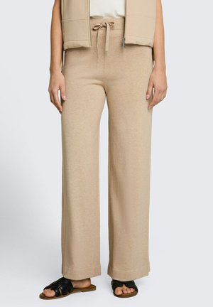 Beige Strickhose mit weitem Bein und Kordelzug in der Taille, kombiniert mit einer beigen Weste, weißem Top und schwarzen offenen Zehen-Slides.