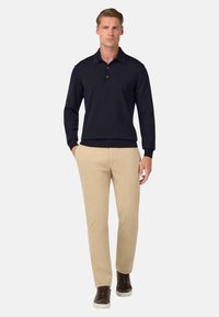 Jūras spēku adīta polo krekls ar apkakli un trim pogām, apvienots ar bēšiem chinos šortiem un brūniem sporta apaviem ar baltām zole.