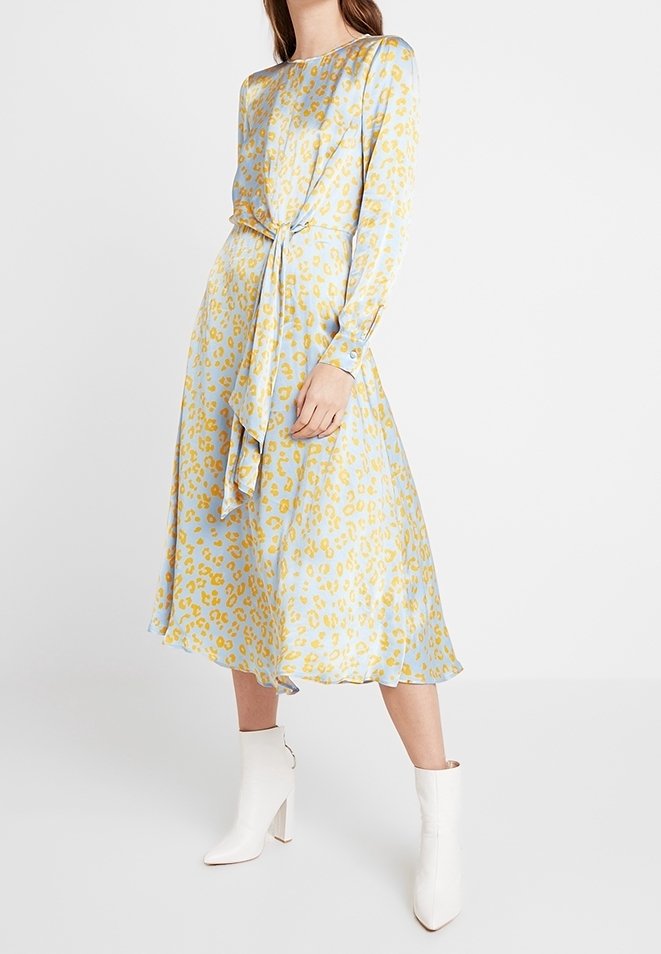 Vaalean sininen pitkähihaisessa mekossa on keltainen leopardikuvio, jossa on solmittava vyötärödetail ja virtaava siluetti, yhdistettynä valkoisiin nilkkasaappaisiin.