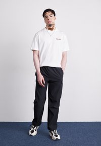 Hvid kortærmet t-shirt med lille brun Timberland-logo, parret med sorte cargo-bukser og sort-hvide sneakers.