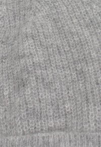 Berretto grigio lavorato a maglia realizzato con filato morbido. Presenta una texture a costine con un aspetto leggermente stirato, che mostra variazioni di grigio chiaro e scuro.