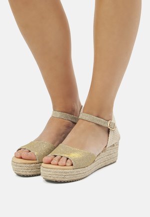 Sandalias de cuña espadrille de hilo de oro, con una amplia correa en los dedos, hebilla en el tobillo y suela de yute natural. Textura suave, diseño abierto.