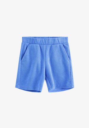 Dreng går fremad iført blå kortærmet skjorte med krave, matchende shorts, hvide sneakers og hvide sokker med blå striber mod en ensfarvet baggrund.