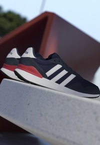 Zapatillas Adidas azul marino y blanco con detalles en rojo, exhibidas sobre una superficie de hormigón con un fondo exterior.