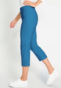 Blauwe cropped broeken met een gladde stofafwerking, met een hoge taille en zijsplitsdetails, gecombineerd met witte sneakers.