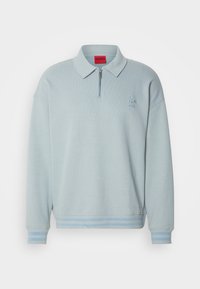 Pull bleu clair à manches longues avec col, fermeture éclair au quart, poignets et ourlet côtelés avec des rayures, et logo brodé subtil sur la poitrine gauche.