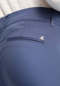 Slim-fit tmavě modré kalhoty vyrobené z hladké tkaniny, s jednou zadní kapsou a malým stříbrným logem jako akcentem. Ušito s čistým designem.