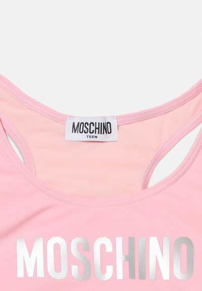 Κοντινή λήψη ενός ροζ αμάνικου τοπ για εφήβους Moschino με ασημένιο όνομα της μάρκας τυπωμένο στο στήθος και ετικέτα ραμμένη στο εσωτερικό μέρος του λαιμού.