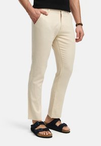 Beige cotton pants with side pockets and a straight leg cut, paired with black sandals featuring two adjustable straps and a cork sole.