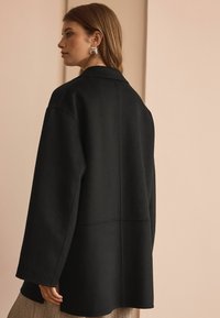 Svart ull-blandad kappa med en något oversized passform, som har en notchad krage och minimalistisk design. Strukturerad tyg med mjuk finish.