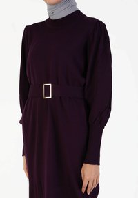 Langärmliges, lila Kleid aus weichem Stoff, mit einem gerippten Ausschnitt und einem Stoffgürtel mit einer rechteckigen goldenen Schnalle.