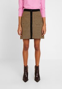 Jupe à motif pied-de-poule beige et noir, avec une ceinture noire, des boutons sur le devant et deux grandes poches avant.