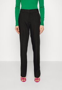 Svarta skräddarsydda byxor med rak passform och mjuk yta, kombinerat med en grön långärmad topp och rosa sandaler med remmar.