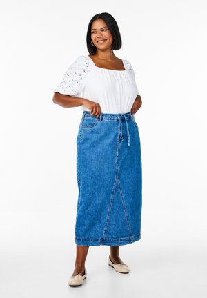 Modrá denimová sukňa s vysokým pásom, predným viazaním a voľným strihom, spárovaná s bielou blúzkou s krátkym rukávom a očkovými vzormi.