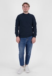 Felpa navy a maniche lunghe con scollo a girocollo, abbinata a jeans slim-fit azzurri e sneakers bianche. Design semplice e strutturato.