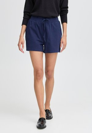Shorts en coton bleu marine avec une taille élastique et un cordon de serrage, présentant une coupe décontractée et sans motifs visibles. Associés à des chaussures noires.