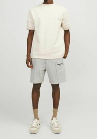 Pantalones cortos de algodón gris claro con cordón, combinados con una camiseta de manga corta color crema. Completados con zapatillas deportivas beige y calcetines.