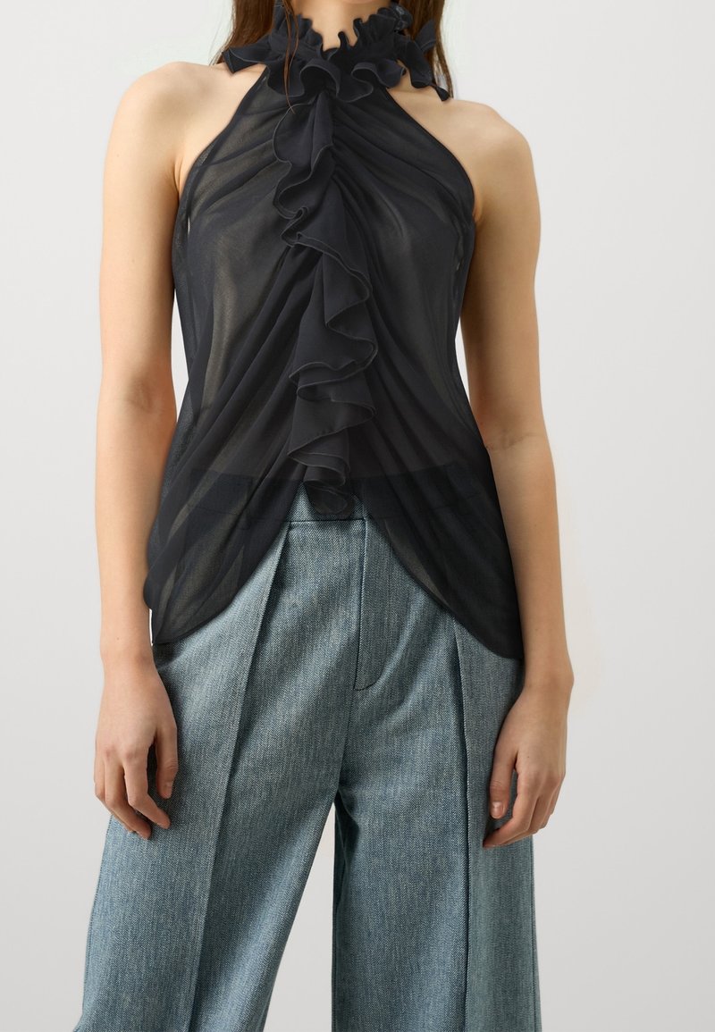 Top halter negro transparente con escote con volantes y un diseño fluido. Combinado con pantalones de pierna ancha texturizados en azul claro.