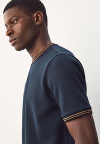 Maglia in maglia testurizzata blu navy con colletto e polsini a righe a contrasto. Maniche corte, scollo tondo e silhouette aderente.