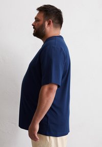 T-shirt à manches courtes bleu marine avec une coupe décontractée, un col rond et une texture lisse, associé à un pantalon de couleur crème.