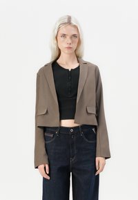 Kuttet brun blazer med en jevn tekstur, to frontlommer, notched revers, kombinert med en svart henley topp og mørke denimjeans.