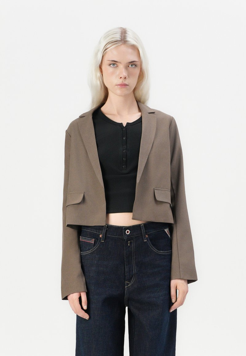 Kuttet brun blazer med en jevn tekstur, to frontlommer, notched revers, kombinert med en svart henley topp og mørke denimjeans.