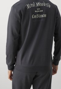 Felpa grigia scura con maniche lunghe, con la scritta "Real Madrid" e disegni sul retro, realizzata in tessuto morbido con una vestibilità comoda.