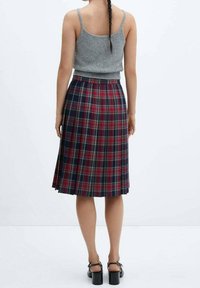 Haut tricoté gris et jupe à carreaux longueur genou avec des couleurs rouge, marine et crème. La jupe présente des plis et une ceinture élastique.