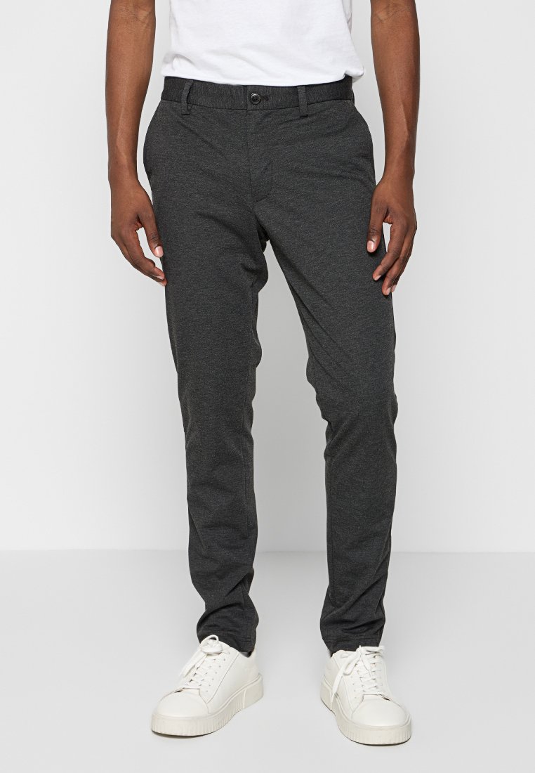 Męskie ciemnoszare chinosy wykonane z gładkiego materiału o zwężanym kroju, z zapięciem na guzik i bocznymi kieszeniami, w połączeniu z białymi trampkami.