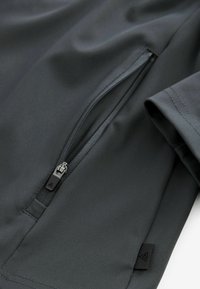 Chaqueta deportiva gris oscuro con un bolsillo con cremallera, textura suave y un diseño elegante con acentos minimalistas.