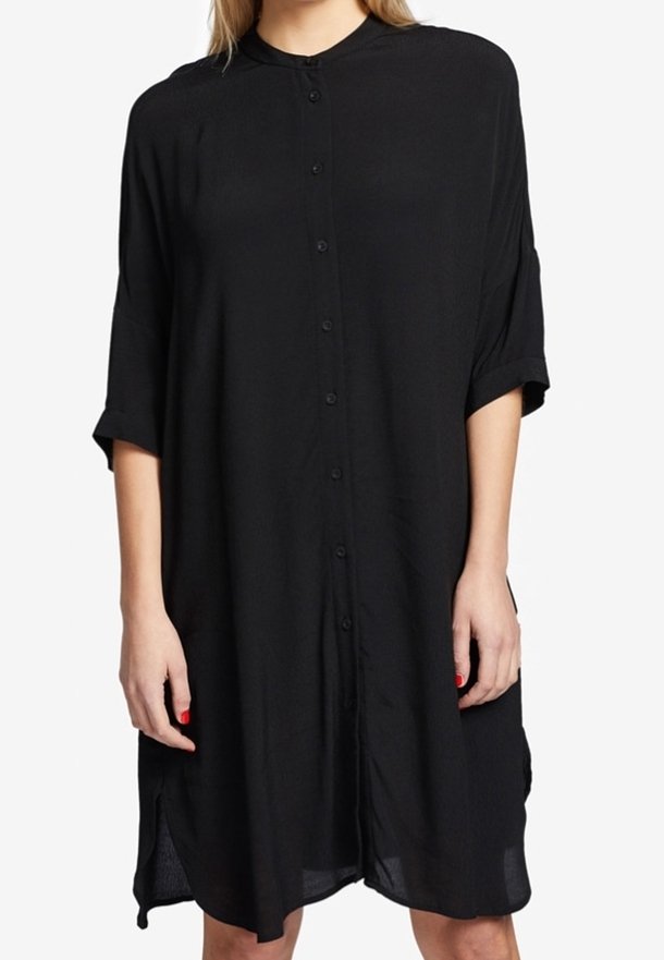 Svart knappuppklädd klänning med krage, korta ärmar och sidokläppar. Tillverkad av lätt material med en mjuk textur. Längden når mitt på låret.