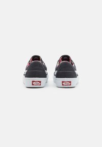 Un paio di sneakers Vans nere con suole bianche viste di spalle, caratterizzate dai loghi "Off The Wall" sulle linguette del tallone e da una fodera interna colorata.